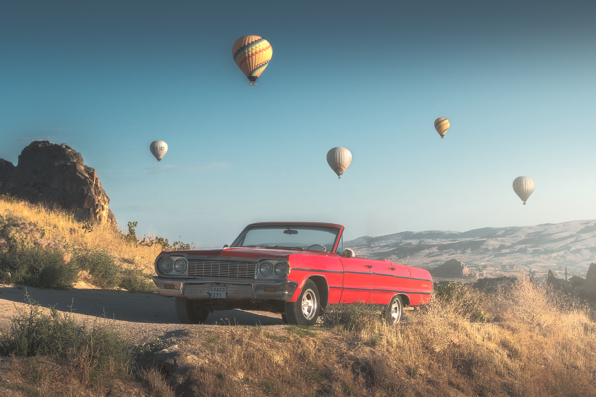 Red vintage car overlooking hot air balloons above the landscape of Cappadocia