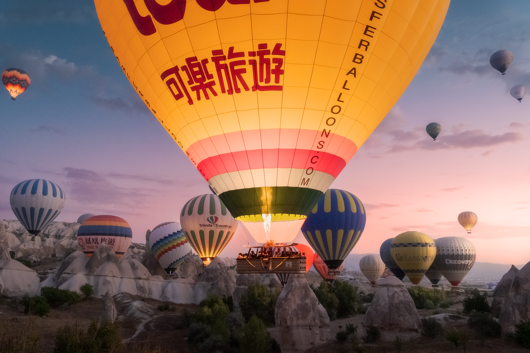 Large hot air balloon rising among dozens of balloons over Cappadocia at dawn