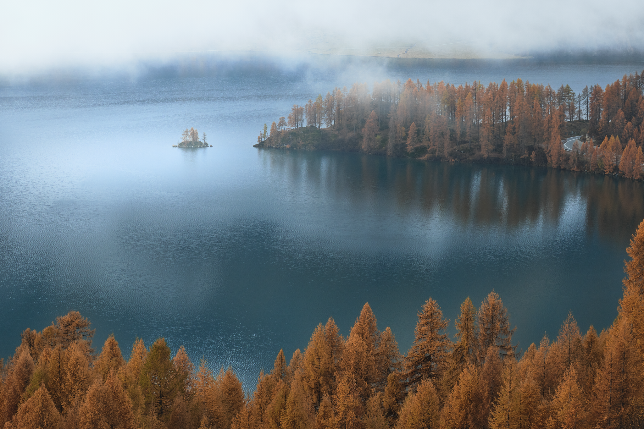 Small island surrounded by turquoise water and autumn larch trees in Switzerland