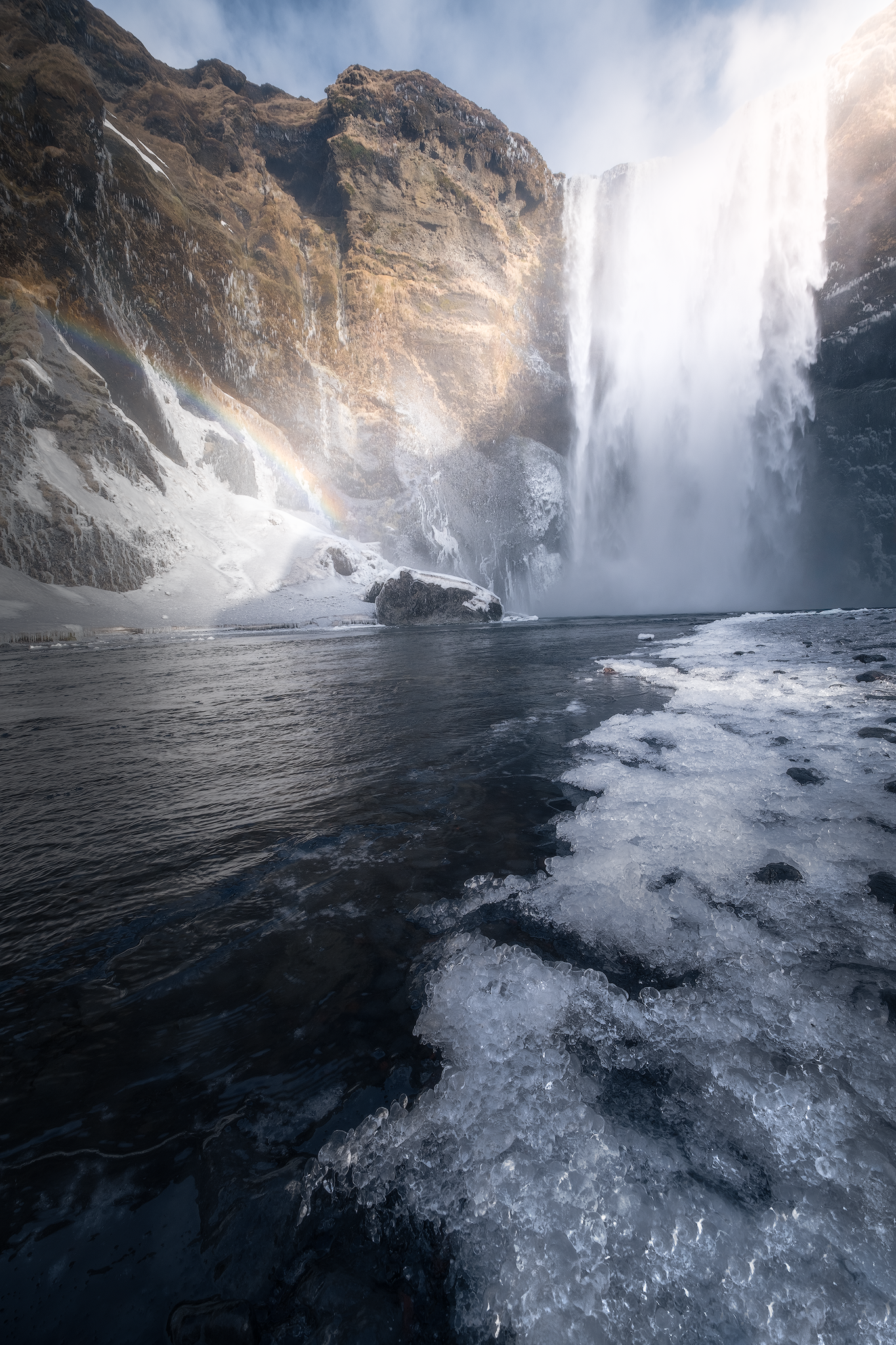 Frozen Icelandic waterfall surrounded by ice, dark rock and winter light