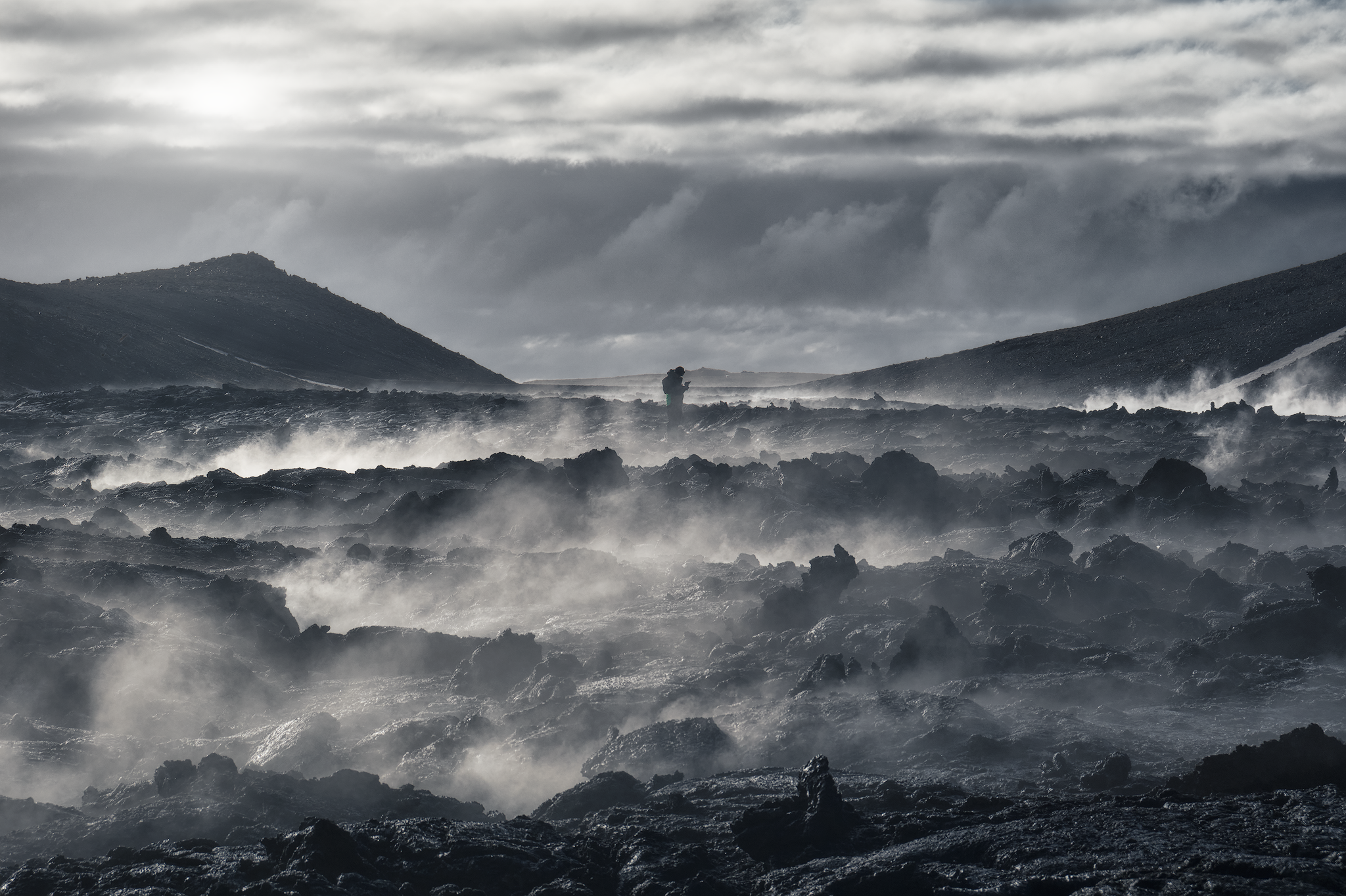 Traveller standing among steaming lava rocks beneath a dramatic Icelandic sky