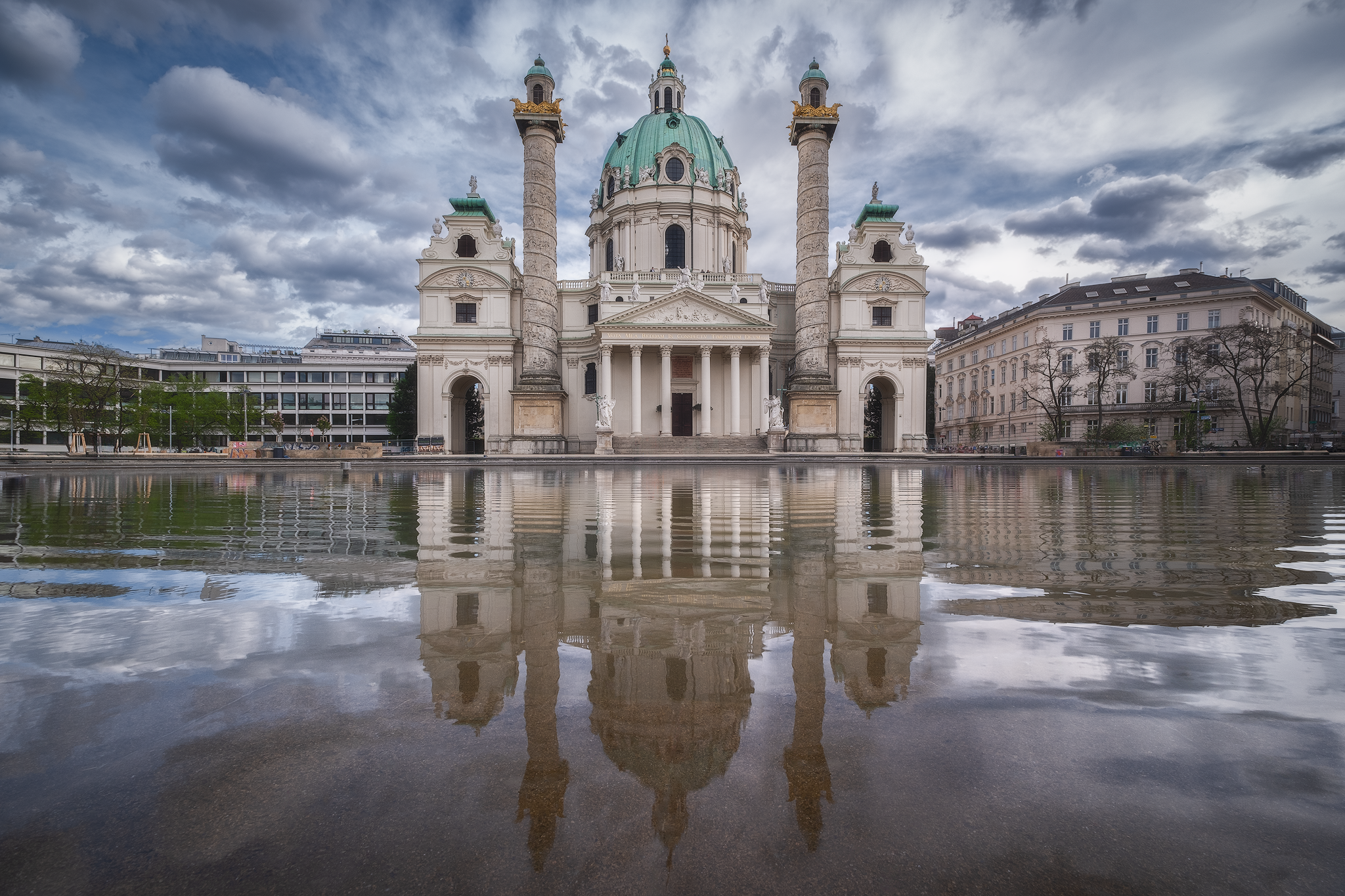 Karlskirche reflected in water beneath dramatic clouds in Vienna